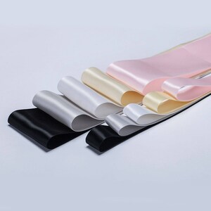 May include: A set of six satin ribbons in various colors, including black, white, cream, and pink. The ribbons are arranged in a fan shape, with the black ribbon at the bottom and the pink ribbon at the top.
