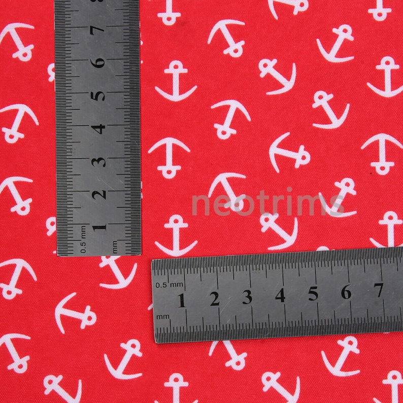May include: Red fabric with a white anchor pattern. The fabric is measured with two rulers, one in inches and one in centimeters.