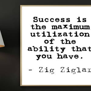 Puede incluir: Una lámpara de mesa blanca con una pantalla interior dorada se encuentra junto a una impresión enmarcada. La impresión presenta la cita "Success is the maximum utilization of the ability that you have." de Zig Ziglar, en texto negro.