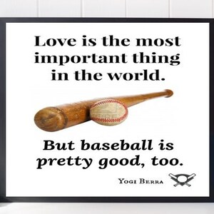 May include: A black framed print with a white background and a baseball quote by Yogi Berra. The quote reads "Love is the most important thing in the world. But baseball is pretty good, too."