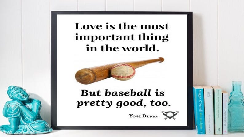 May include: A black framed print with a white background and a baseball quote by Yogi Berra. The quote reads "Love is the most important thing in the world. But baseball is pretty good, too."