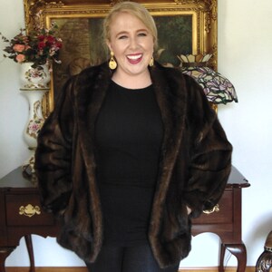 May include: A woman wearing a brown faux fur jacket over a black long-sleeved shirt and black leggings. She is smiling and has gold earrings.