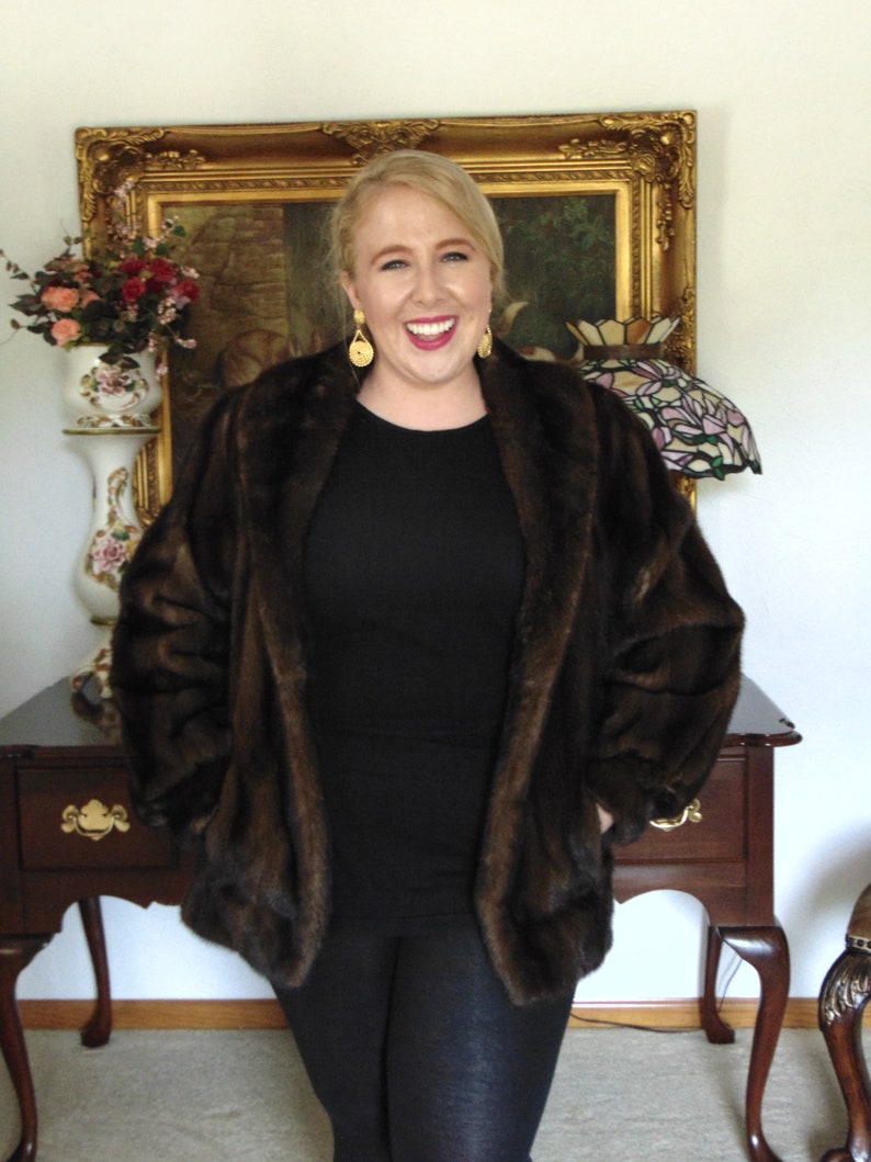 May include: A woman wearing a brown faux fur jacket over a black long-sleeved shirt and black leggings. She is smiling and has gold earrings.