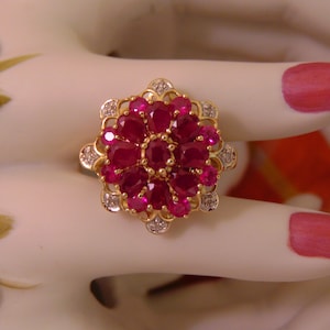 May include: A gold ring with a cluster of red rubies and small diamonds set in a floral design.