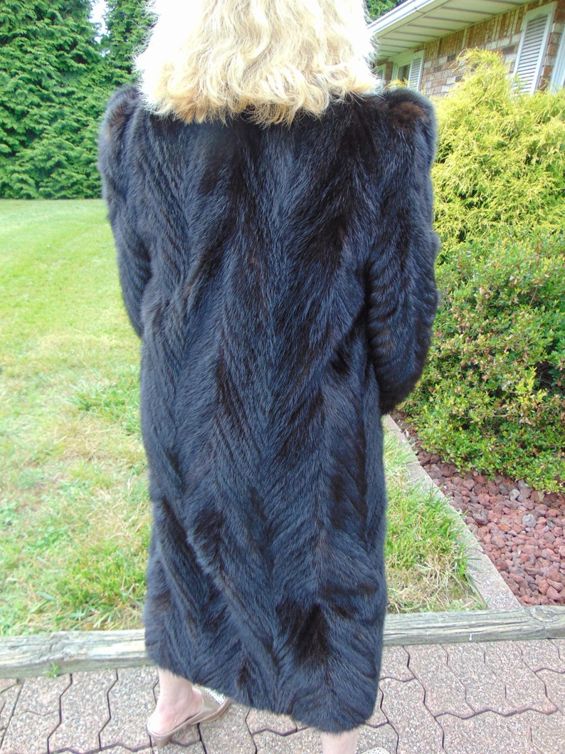 May include: A long black fur coat with a chevron pattern. The coat is made of a soft, luxurious fur.