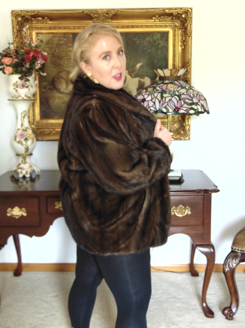 May include: A woman wearing a brown fur coat with a stained glass lamp in the background.