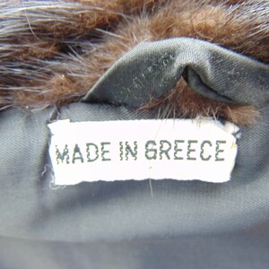 May include: A white tag with the text "MADE IN GREECE" sewn into a brown fur coat.