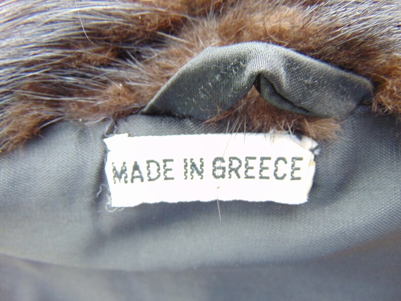 May include: A white tag with the text "MADE IN GREECE" sewn into a brown fur coat.