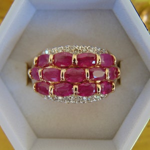 May include: A gold ring with a band of small diamonds and three rows of oval-shaped ruby stones.