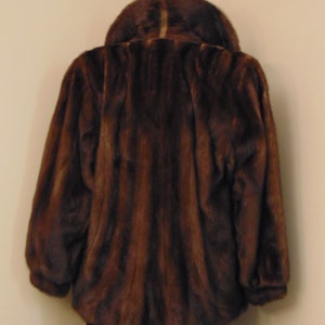 May include: A brown fur jacket with a collar. The jacket is on a mannequin and the background is a light beige wall.