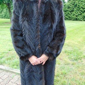 May include: A long, dark brown fur coat with a chevron pattern. The coat has a high collar and long sleeves.