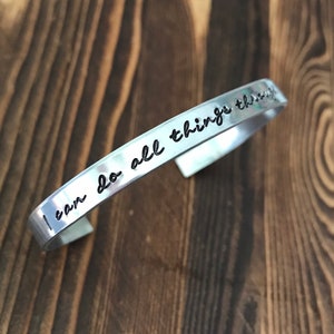 May include: Silver bracelet with the inscription "I can do all things through Christ" on a wooden background.