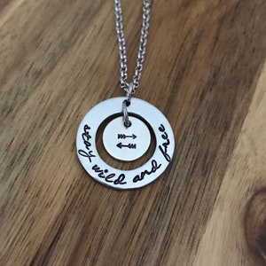 May include: A silver necklace with a round pendant that says "stay wild and free" with arrows in the center.