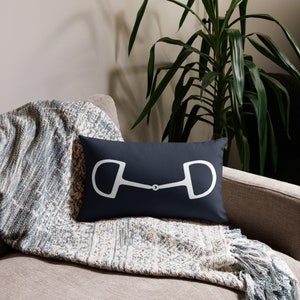 May include: A navy blue throw pillow with a white outline of a horse bit. The pillow is on a couch with a blue and white throw blanket.