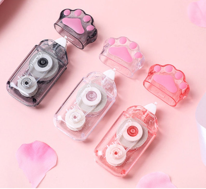 May include: Four clear plastic tape dispensers with paw print designs. Each dispenser has a clear tape roll and a small, clear paw print on the top. The dispensers are on a pink surface.