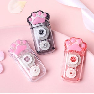 May include: Three clear plastic tape dispensers shaped like a paw print. Each dispenser has a pink paw print on the front and a clear tape roll inside.