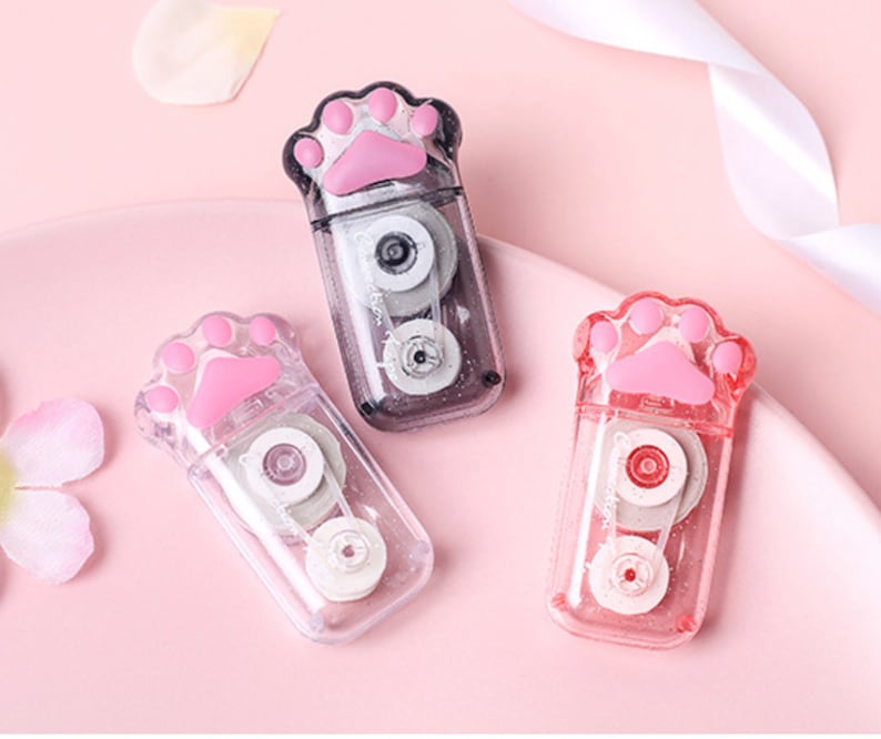 May include: Three clear plastic tape dispensers shaped like a paw print. Each dispenser has a pink paw print on the front and a clear tape roll inside.