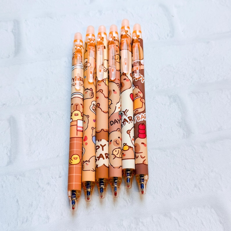 May include: Seven brown and tan pens with cartoon bear designs. The pens have a variety of bear illustrations and the words "Happy Day" printed on them. The pens have orange accents and blue ink tips.