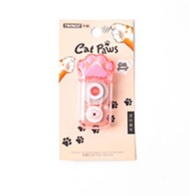May include: A pink and clear plastic tape dispenser shaped like a cat paw. The dispenser has a black paw print on the front and the words "Cat Paws" in black text.