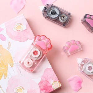 May include: Five pink and clear plastic tape dispensers with paw print designs. The dispensers are on a pink background with pink watercolour flowers.