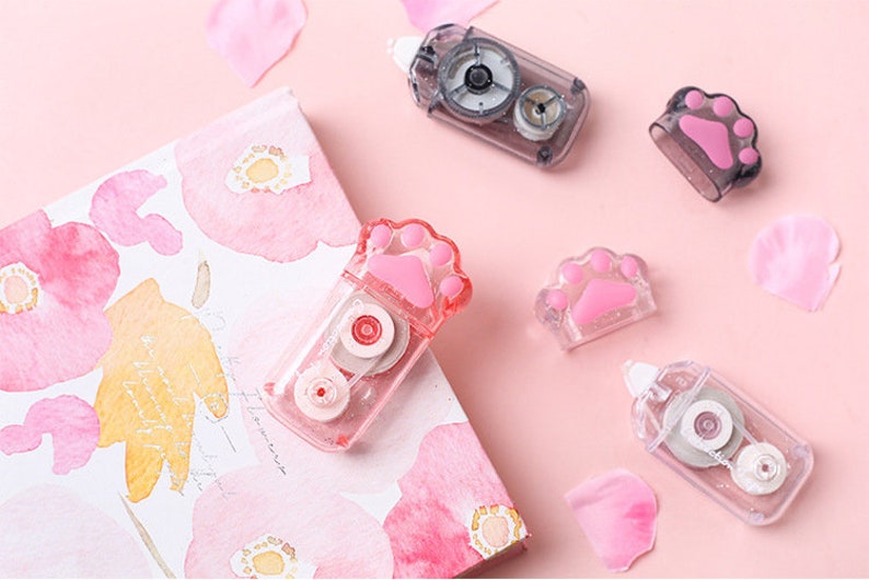 May include: Five pink and clear plastic tape dispensers with paw print designs. The dispensers are on a pink background with pink watercolour flowers.