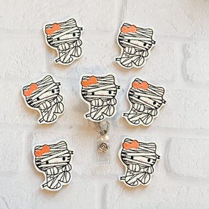 May include: Seven white embroidered mummy Hello Kitty patches with orange bows. The patches are on a white surface with a brick pattern.