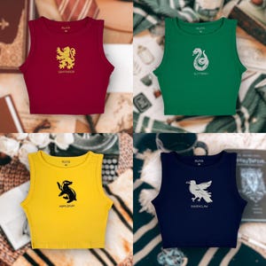 May include: Four crop tops in red, green, yellow, and navy blue. Each top features a house crest and name from a fantasy series. The red top has a gold lion and the word "Gryffindor". The green top has a silver snake and the word "Slytherin".
