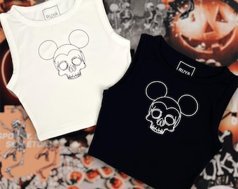 Puede incluir: Dos tops cortos sin mangas, uno blanco y otro negro, con un diseño de calavera con orejas de Mickey Mouse. Las camisetas tienen la palabra "RUYA" impresa en la etiqueta. El fondo incluye decoraciones temáticas de Halloween.