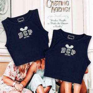 May include: Two navy blue sleeveless crop tops with a white Mickey Mouse ear logo and the text "DCP EST 1981".