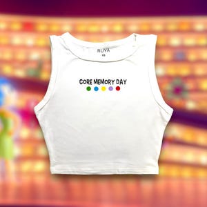 Peut inclure: Top court blanc sans manches avec le texte "CORE MEMORY DAY" et cinq points colorés en dessous. Le nom de la marque "RUYA" et la taille "XS" sont imprimés sur l'étiquette.