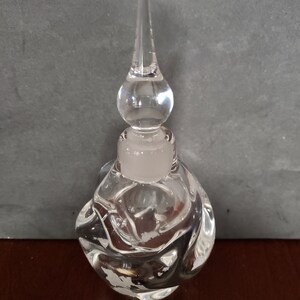 May include: A clear glass bottle with a textured, bulbous body and a tall, pointed stopper. The bottle has a frosted white top.