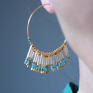 May include: Gold hoop earrings with a fringe of turquoise and clear beads hanging from the bottom.
