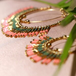 May include: A pair of large hoop earrings with a fringe of pink and green beads. The earrings are made of gold metal and have a delicate, bohemian style.
