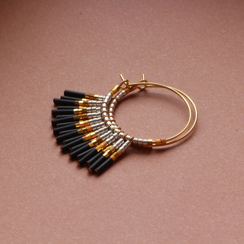 May include: Gold hoop earrings with black and silver beads. The beads are arranged in a fan shape and hang from the hoop.