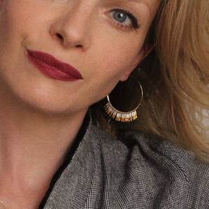 May include: A woman wearing a grey blazer with gold hoop earrings featuring black and white beads dangling from them. The earrings are a statement piece and add a touch of elegance to the outfit.