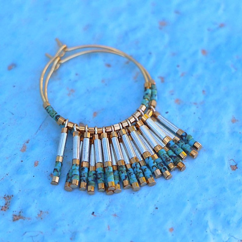 May include: Gold hoop earrings with a turquoise and silver fringe. The fringe is made of small, cylindrical beads.