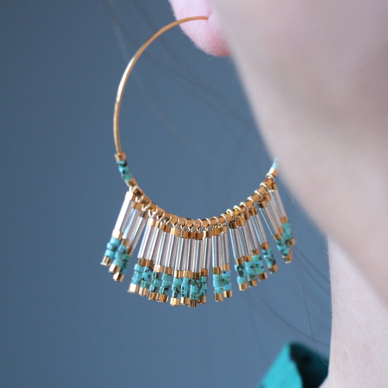 May include: Gold hoop earrings with a fringe of turquoise and clear beads hanging from the bottom.