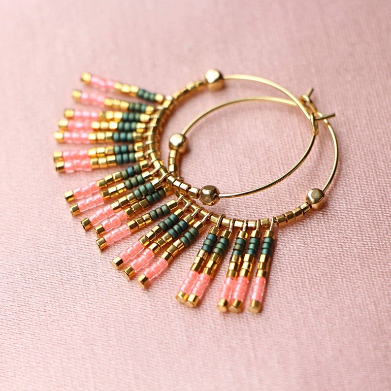 May include: Gold hoop earrings with pink and green beaded fringe. The fringe is made of small, round beads that hang from the hoop.