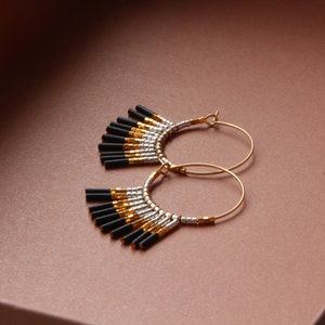 May include: Gold hoop earrings with black and silver beads hanging from the bottom. The beads are arranged in a fan shape.