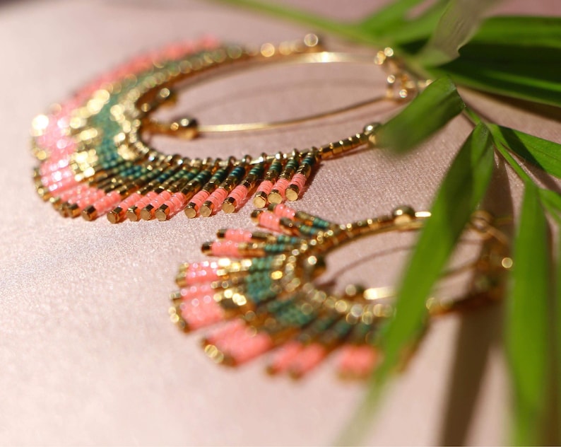 May include: A pair of large hoop earrings with a fringe of pink and green beads. The earrings are made of gold metal and have a delicate, bohemian style.