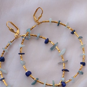 Peut inclure: Boucles d'oreilles créoles dorées avec des éclats de pierres précieuses bleues et bleu clair.