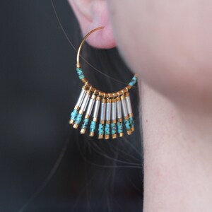 May include: Gold hoop earrings with a fringe of turquoise and silver beads.