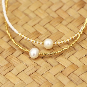 May include: Two strands of beaded necklaces with white and gold beads. The necklaces feature two white pearl accents.