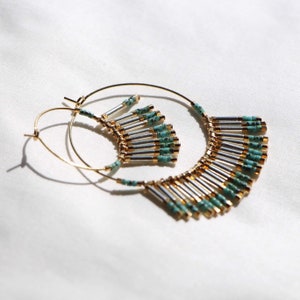 May include: Gold hoop earrings with a turquoise and silver beaded fringe. The fringe is made of small, cylindrical beads that are strung together in a cascading pattern.