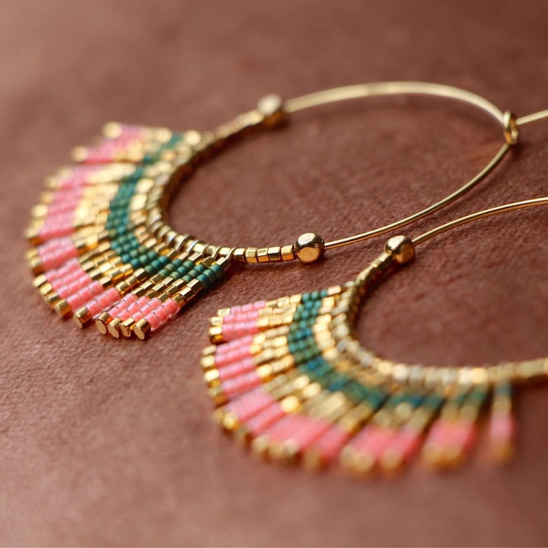 May include: Gold hoop earrings with pink and green beaded fringe. The fringe is made of small, colorful beads that hang from the hoop.