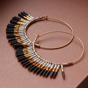 May include: Gold hoop earrings with black and silver beads hanging from the bottom. The beads are arranged in a graduated pattern, with the longest beads at the bottom.