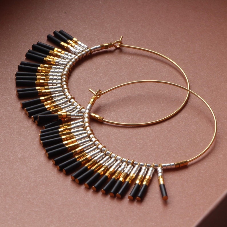 May include: Gold hoop earrings with black and silver beads hanging from the bottom. The beads are arranged in a graduated pattern, with the longest beads at the bottom.