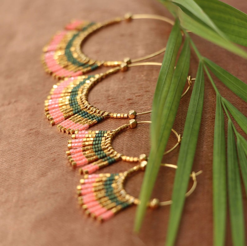 May include: Three pairs of gold hoop earrings with pink and green beaded fringe. The earrings are arranged in a cascading pattern, with the largest pair at the top and the smallest pair at the bottom.