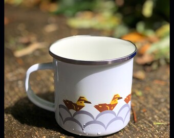 May include: White enamel mug with a blue and brown design of stylized birds. The mug has a silver rim and a handle.