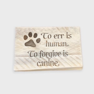 May include: A wooden sign with a paw print and the text "To err is human, To forgive is canine."